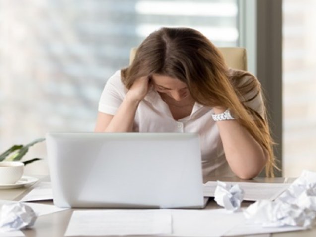 Desperate businesswoman sitting at the desk with laptop and crumpled paper. Female office worker suffers because of too much mess in her thoughts. Stressed woman entrepreneur feeling creativity crisis